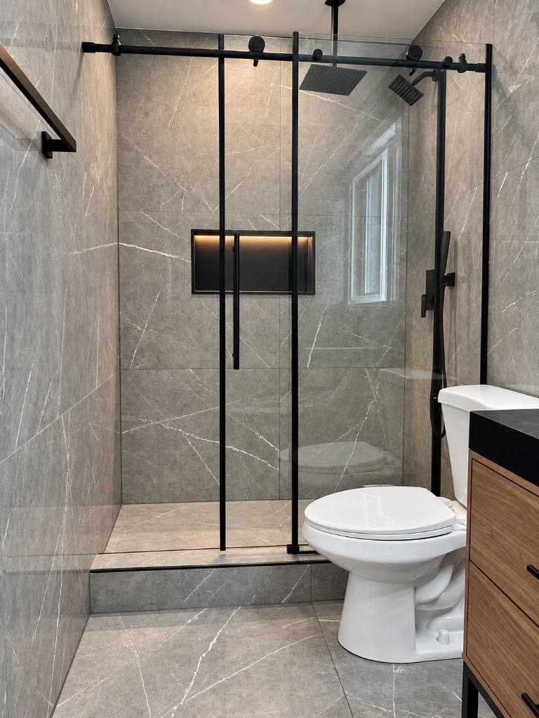 Gray marble tile walk-in shower with black glass doors